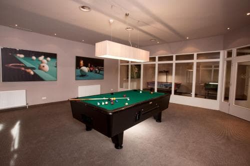 A cozy indoor recreation room features a pool table under modern lighting, framed by large windows and wall art, ideal for travelers seeking relaxation and entertainment in a private setting.