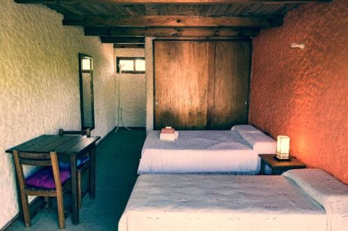 A cozy rustic bedroom with two neatly made beds, warm-toned walls, wooden furniture, and soft lighting creates an inviting atmosphere ideal for travelers seeking a tranquil retreat.