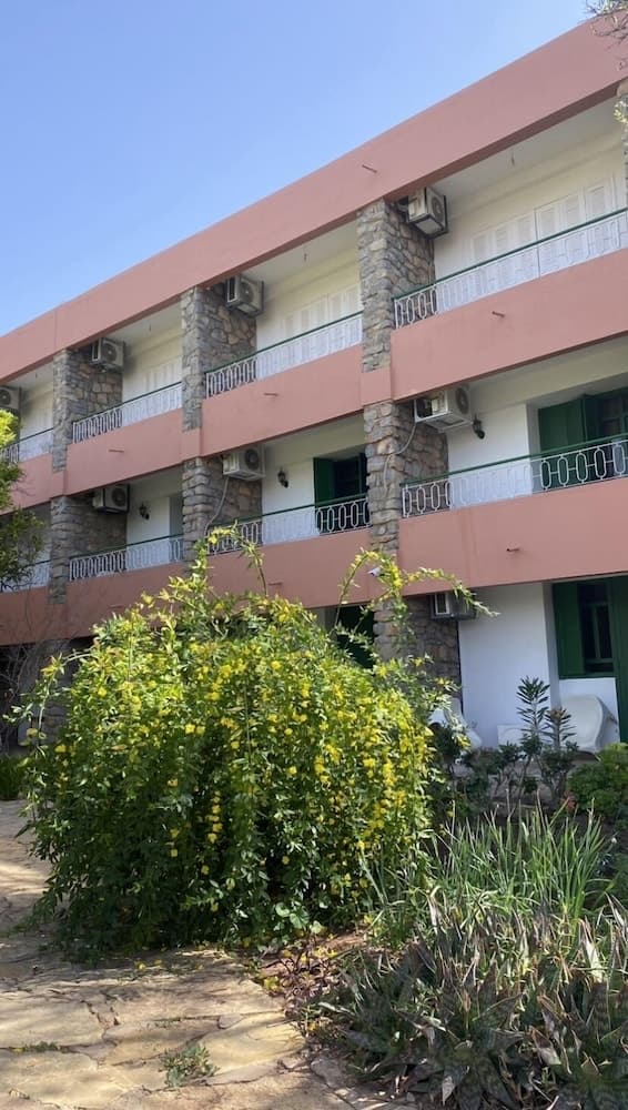 A serene hotel exterior with terracotta balconies, stone pillars, and lush greenery offers a tranquil retreat for travelers seeking relaxation.