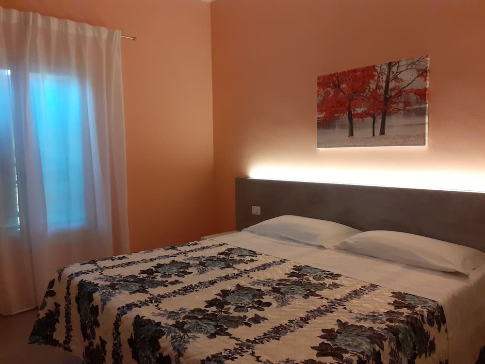 A cozy hotel room with warm orange walls, a floral-patterned bedspread, and an autumn-themed artwork creates a serene atmosphere ideal for travelers seeking relaxation.