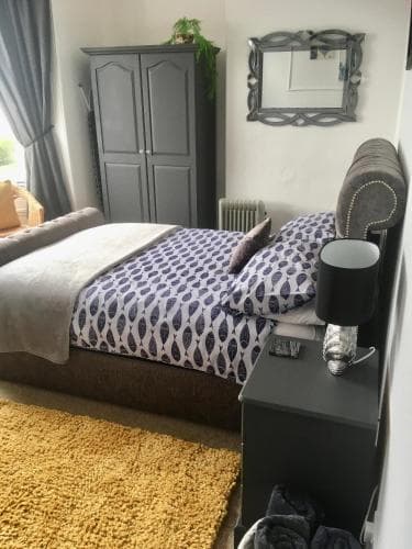 A cozy bedroom with a neatly made bed adorned in blue patterns, a yellow rug, and modern furnishings creates a welcoming atmosphere ideal for travelers seeking comfort and relaxation.