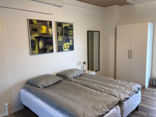 A cozy bedroom with a neatly made bed, abstract wall art, and modern furnishings offers a serene retreat for travelers seeking comfort in a minimalist apartment setting.