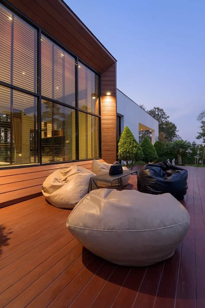 A serene evening on a modern wooden deck features cozy bean bags and sleek glass walls, ideal for travelers seeking relaxation in a contemporary outdoor setting.