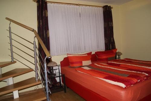 A cozy bedroom with vibrant red bedding, a staircase leading to an upper level, and large curtains covering the window, ideal for travelers seeking comfort in a compact living space.
