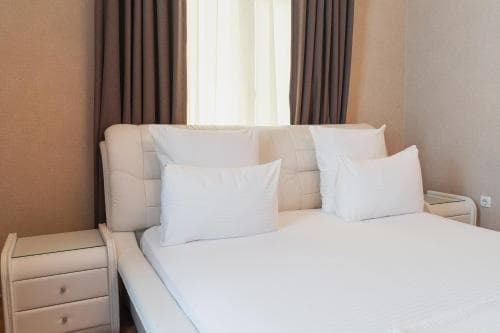 A cozy hotel room features a neatly made bed with white linens, flanked by modern bedside tables under soft natural light filtering through curtains, ideal for travelers seeking comfort and relaxation.
