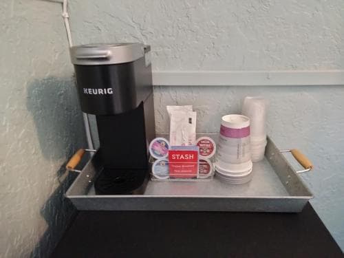 A cozy hotel room coffee station featuring a Keurig machine, tea packets, and disposable cups on a metal tray, perfect for travelers seeking convenience and comfort during their stay.