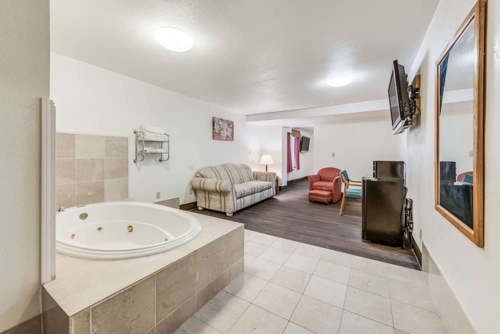 A cozy hotel suite featuring a tiled jacuzzi tub, comfortable seating area, flat-screen TV, and modern amenities, ideal for travelers seeking relaxation and convenience.