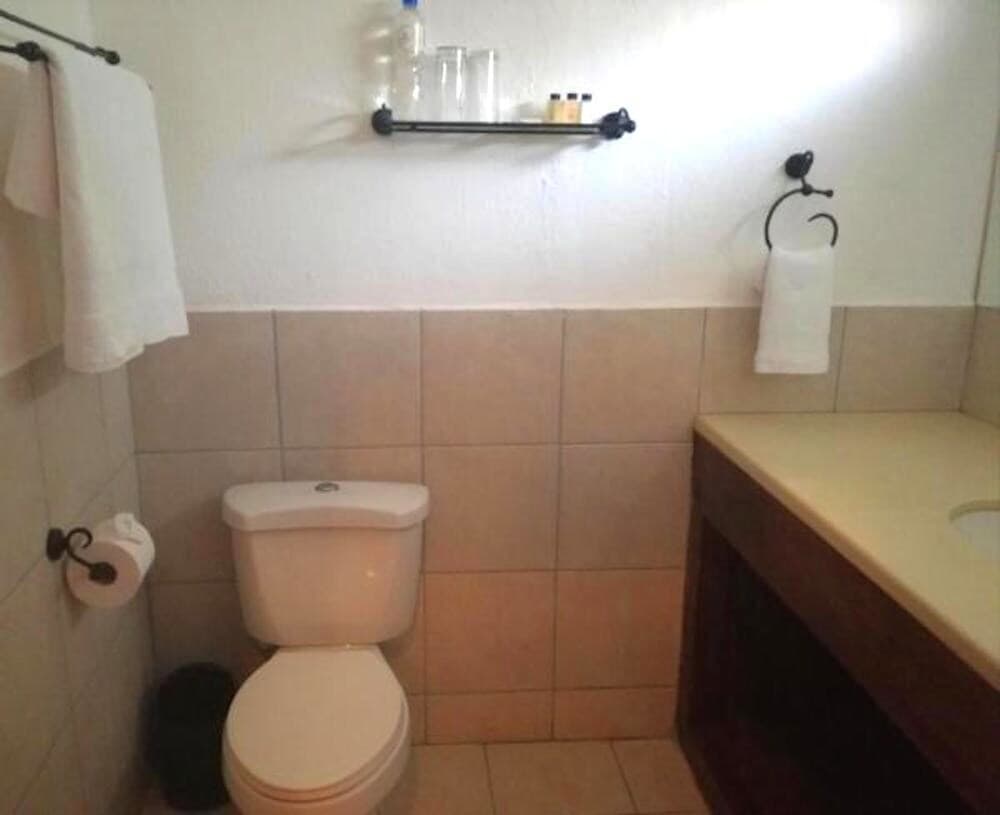 A cozy hotel bathroom features beige tiled walls, a white toilet, a wooden vanity with a sink, and neatly arranged towels, ideal for travelers seeking comfort and cleanliness.