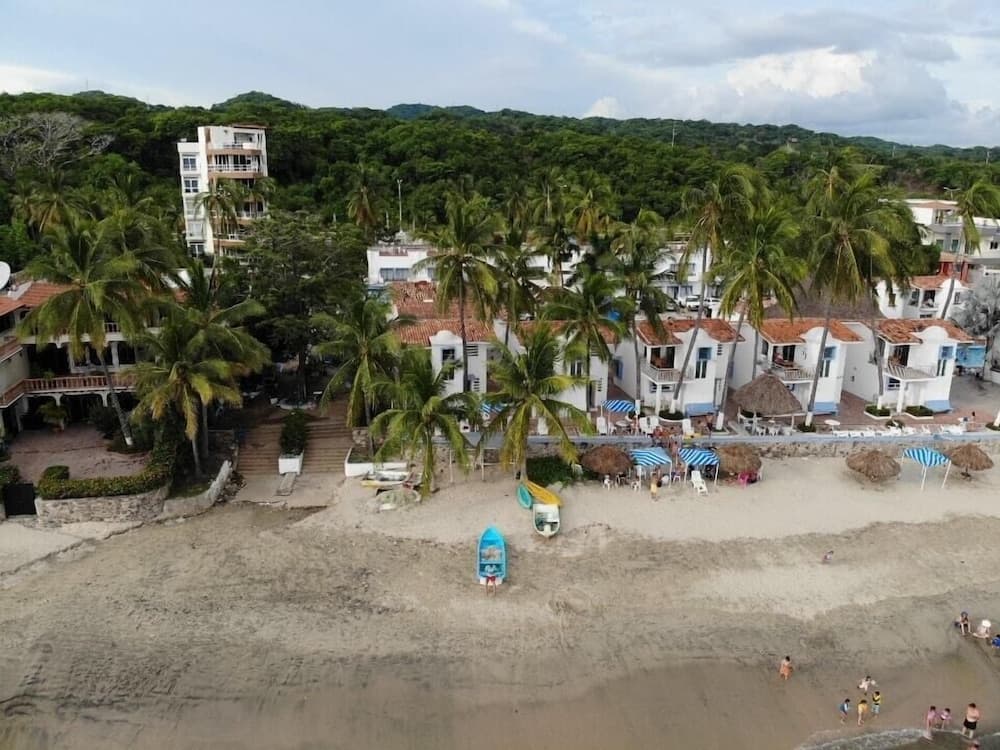 A serene tropical beach scene features sandy shores lined with palm trees, colorful umbrellas, and white buildings with red roofs, ideal for a relaxing vacation getaway.