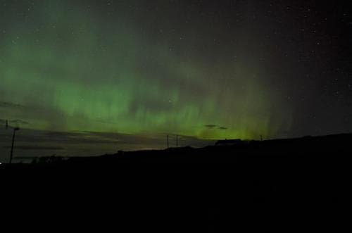 A serene night scene captures the mesmerizing Northern Lights dancing above a tranquil landscape, ideal for travelers seeking breathtaking natural phenomena under a starry sky.