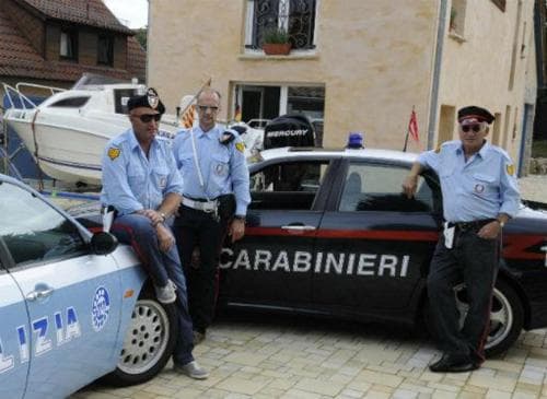 Three officers in uniform stand confidently beside their marked police cars in a quaint village setting, exuding authority and readiness for law enforcement duties.