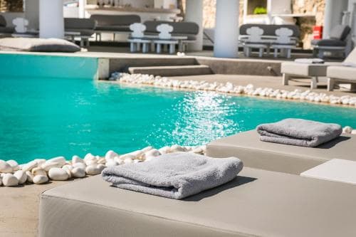 A serene luxury resort poolside scene features plush lounge chairs adorned with neatly folded towels, surrounded by white pebbles, inviting travelers to unwind in a tranquil tropical getaway.