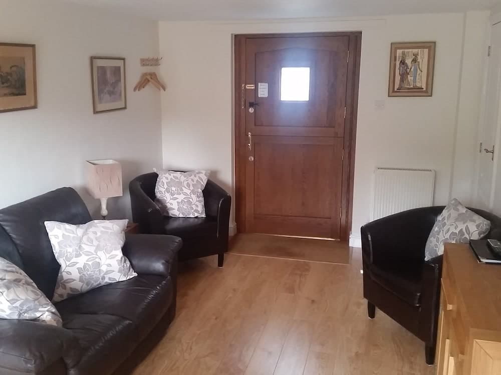 A cozy living room with leather furniture, floral cushions, framed artwork, and a wooden door creates a welcoming atmosphere ideal for travelers seeking a comfortable stay.