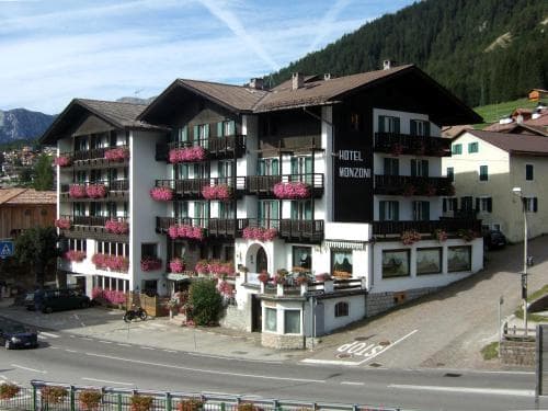 A charming hotel adorned with vibrant flower boxes stands invitingly in a picturesque mountain village, perfect for travelers seeking a cozy retreat amidst nature.