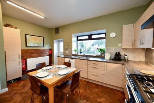 A cozy kitchen with wooden flooring, a dining table set for four, and a window view of greenery, ideal for travelers seeking a homey and functional space for self-catering stays.