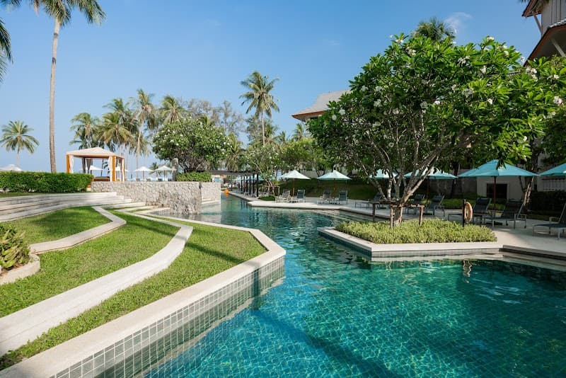 A serene tropical resort scene featuring a crystal-clear pool lined with lush greenery, palm trees, and vibrant turquoise umbrellas, ideal for a relaxing vacation in Thailand.