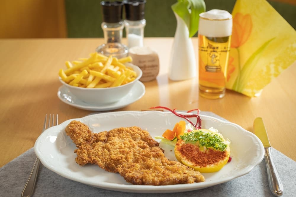 A cozy restaurant table features a crispy schnitzel served with fries, garnished with herbs and lemon, accompanied by a refreshing beer, ideal for travelers seeking traditional European cuisine in a warm, inviting setting.