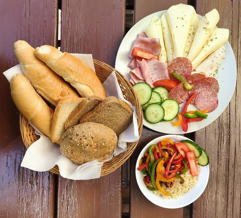 A cozy outdoor dining setup at Sir Toby's Hostel in Prague features a rustic wooden table laden with fresh breads, a colorful charcuterie board, and a vibrant salad bowl, perfect for travelers seeking a relaxed and inviting meal experience.