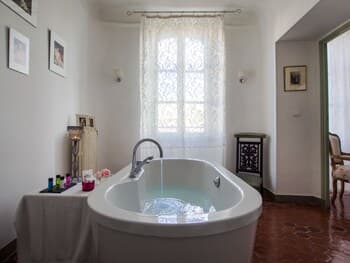 A serene spa room with a freestanding bathtub filled with water, framed by lace curtains and warm terracotta tiles, evokes relaxation and luxury, ideal for travelers seeking a tranquil retreat experience.