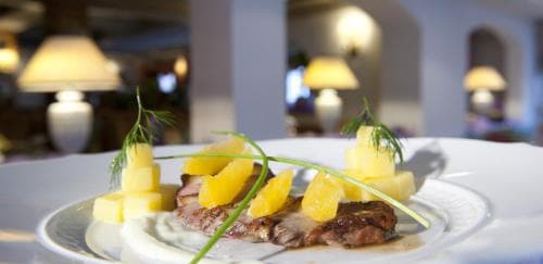 A beautifully plated dish featuring grilled meat garnished with pineapple chunks and herbs is showcased in an elegant restaurant setting, ideal for travelers seeking fine dining experiences.