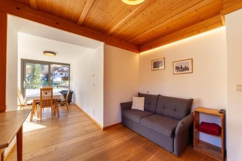 A cozy apartment interior with wooden floors and ceilings, featuring a comfortable gray sofa, dining area by the window, and framed artwork, ideal for travelers seeking a warm and inviting retreat.