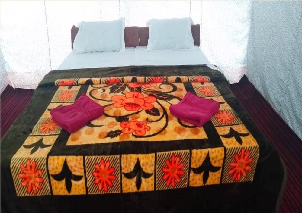 A cozy hotel room features a neatly made bed adorned with a vibrant floral-patterned blanket and folded pink towels, creating a welcoming atmosphere ideal for travelers seeking comfort.