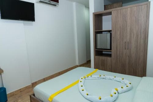 A cozy hotel room features a neatly made bed adorned with a decorative towel swan, wooden furniture, and a mounted TV, ideal for travelers seeking comfort and simplicity.