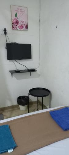 A cozy hotel room features a neatly made bed with folded towels, a small round table, a mounted TV, and a floral poster, creating a simple yet inviting atmosphere ideal for travelers seeking comfort and relaxation.