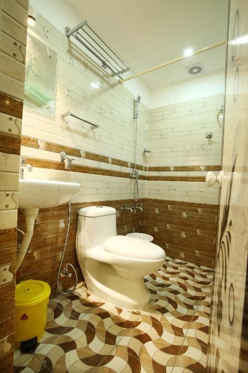 A cozy hotel bathroom features warm-toned tiled walls, a patterned floor, modern fixtures, and a yellow trash bin, ideal for travelers seeking comfort and cleanliness.