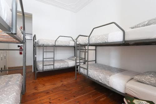 A cozy hostel room with wooden floors, metal bunk beds, and simple decor offers travelers a budget-friendly and communal sleeping arrangement.