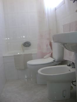 A clean, compact bathroom with white tiled walls, a bathtub, toilet, bidet, and sink creates a serene and functional space ideal for travelers seeking basic amenities in a hotel or guesthouse.