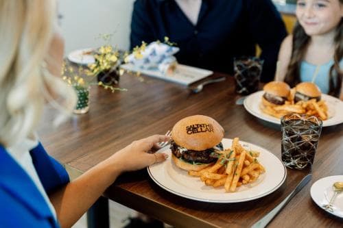 A cozy family dining scene at a casual restaurant features plates of burgers and fries on a wooden table, evoking warmth and togetherness, perfect for travelers seeking a relaxed meal experience.