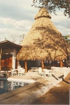 A serene outdoor dining area features a large thatched-roof hut beside a calm pool, ideal for travelers seeking a tranquil tropical retreat experience.