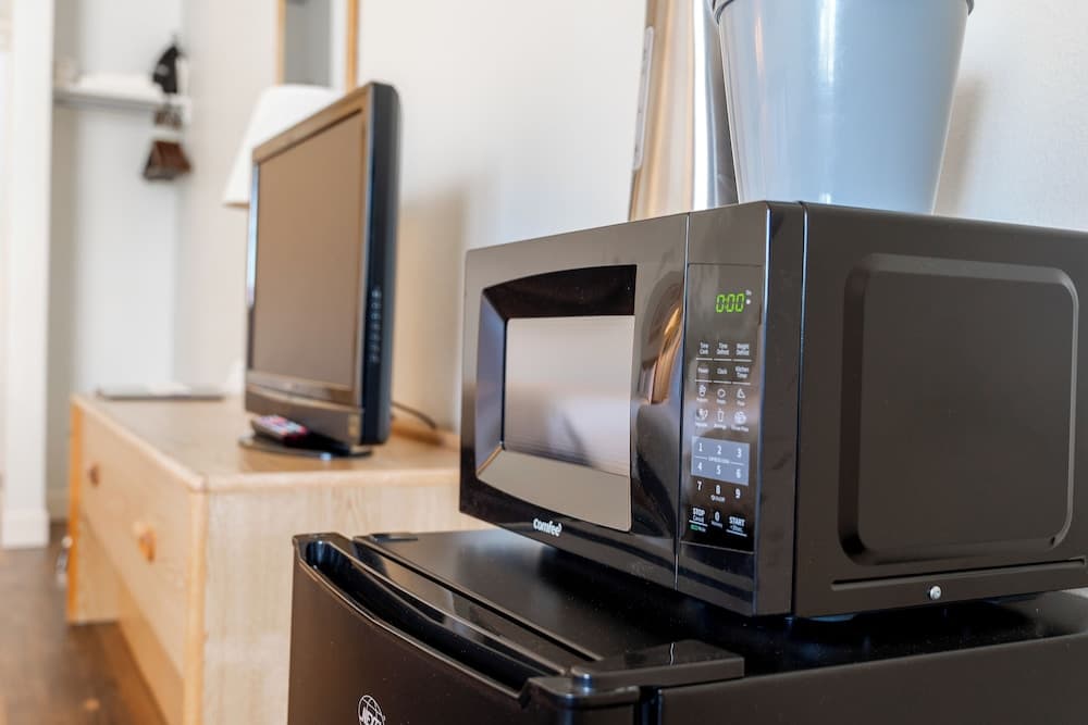 A cozy kitchenette scene featuring a sleek black microwave atop a refrigerator, complemented by a wooden cabinet holding a television and remote, evokes a practical and modern living space ideal for travelers seeking convenience in compact accommodations.
