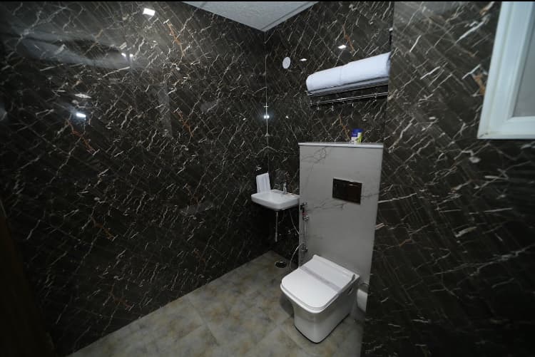 A modern hotel bathroom with sleek black marble walls, a compact toilet setup, and ambient lighting creates an elegant and functional space ideal for travelers seeking comfort in Jaipur, India.