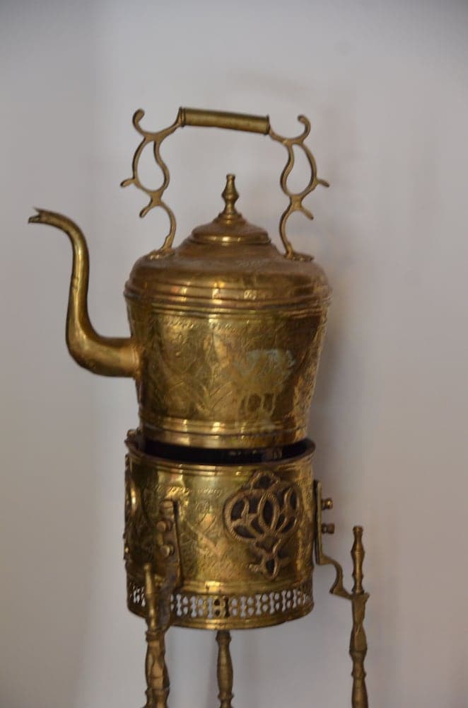 A beautifully crafted brass teapot set on an ornate stand exudes elegance in a minimalist setting, ideal for cultural heritage enthusiasts exploring traditional craftsmanship.