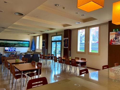 A cozy indoor dining area with wooden tables, red chairs, and large windows offering a serene view, ideal for travelers seeking a comfortable spot to relax and enjoy meals in a modern communal space.