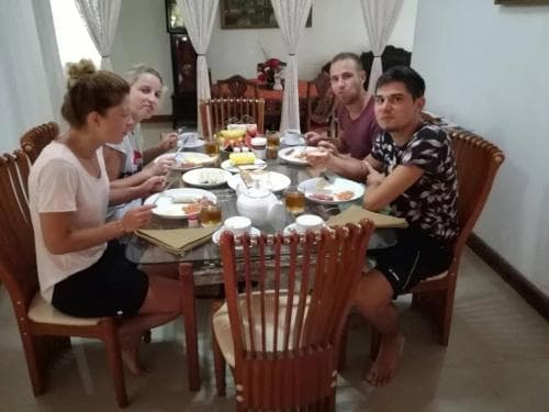 A cozy dining room scene captures travelers enjoying a communal meal around a wooden table adorned with plates of food, creating a warm and inviting atmosphere ideal for group getaways or cultural exchanges.