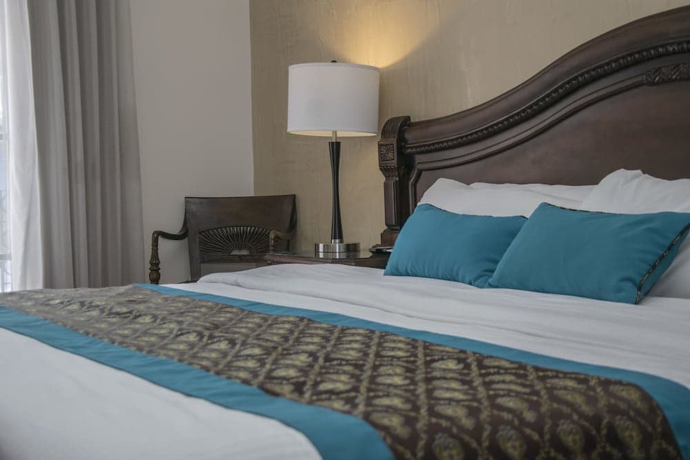 A cozy hotel room features a neatly made bed with teal accents, a stylish wooden headboard, and soft lighting from a bedside lamp, ideal for travelers seeking comfort and relaxation.