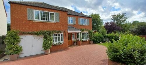 A charming brick house with lush greenery and a welcoming driveway offers a serene suburban retreat, ideal for family vacations or weekend getaways.