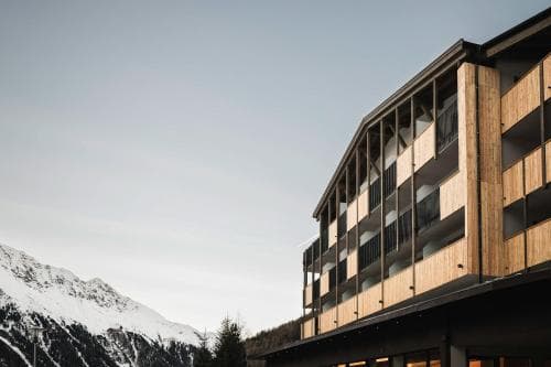 A modern wooden lodge with balconies overlooks a serene snowy mountain landscape, ideal for winter retreats and adventure seekers.