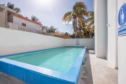 A serene rooftop pool surrounded by white walls and palm trees under a sunny sky offers a tranquil retreat for travelers seeking relaxation in a tropical setting.
