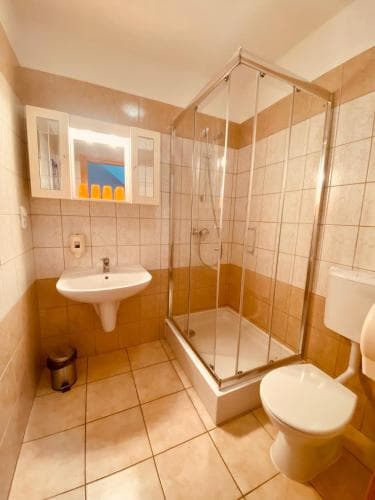 A cozy hotel bathroom features beige tiled walls, a glass-enclosed shower, a sink with a mirrored cabinet, and a toilet, ideal for travelers seeking comfort and cleanliness.