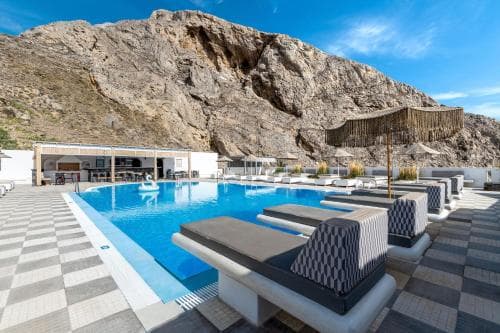A serene luxury resort pool area with lounge chairs and a striking mountain backdrop offers an ideal retreat for relaxation and scenic enjoyment.