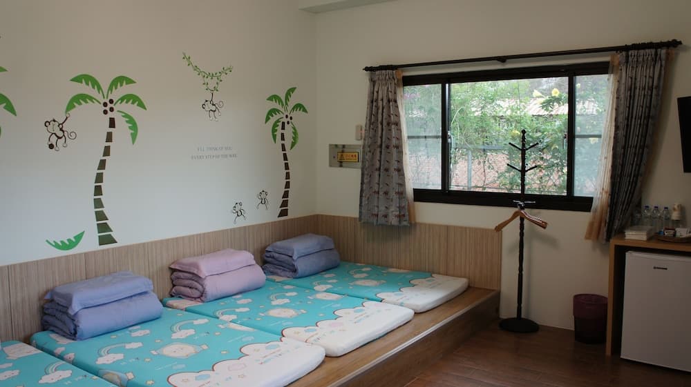 A cozy dormitory room with palm tree wall decals, neatly arranged beds with colorful linens, and a window view of greenery, ideal for budget travelers seeking a cheerful and comfortable stay.