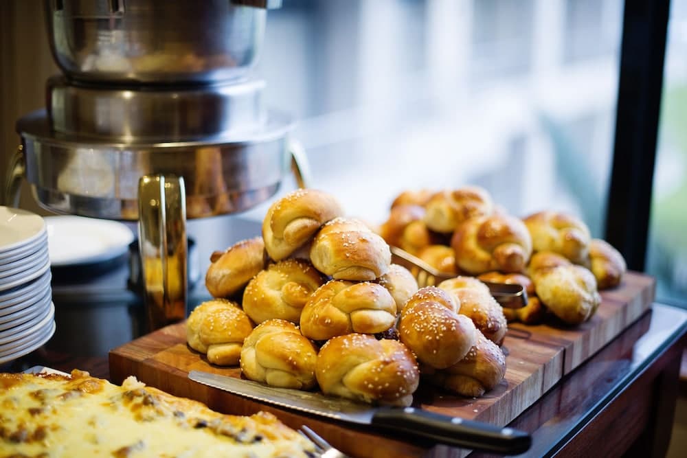 A cozy café scene features a wooden board piled high with golden, sesame-topped pastries next to a sleek coffee maker, inviting travelers to indulge in a warm breakfast or snack.