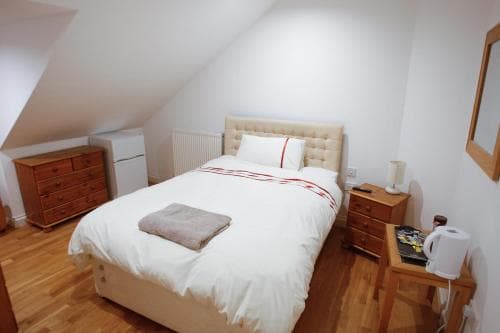 A cozy attic bedroom with sloped ceilings features a neatly made bed, wooden furniture, and soft lighting, ideal for travelers seeking a quiet and comfortable stay.