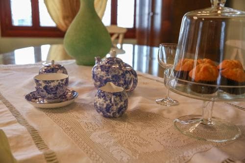 A cozy indoor dining setup features a lace tablecloth, blue-and-white teapots, and a glass-covered pastry display, evoking a serene and inviting atmosphere perfect for a leisurely tea party or breakfast gathering.