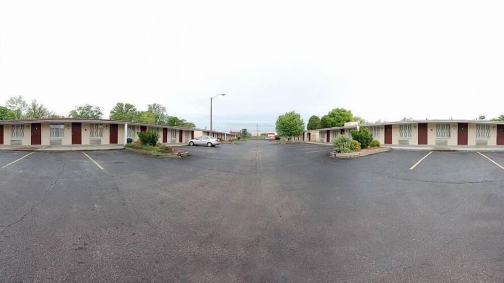 A quiet motel scene features two rows of beige units with red doors, set against a cloudy sky, ideal for travelers seeking budget-friendly accommodations in a serene suburban area.