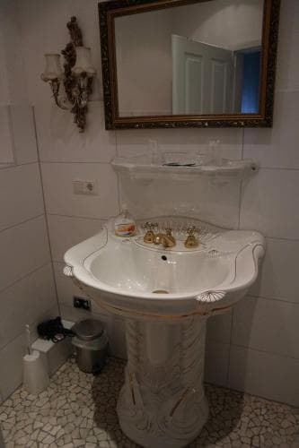 A charming vintage bathroom features an ornate white pedestal sink with gold accents, tiled mosaic flooring, and a decorative mirror, creating an elegant atmosphere ideal for boutique hotel stays or heritage tourism experiences.
